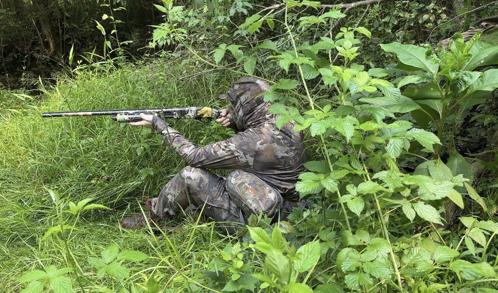 Camouflaged hunter shouldering a shotgun in the field
