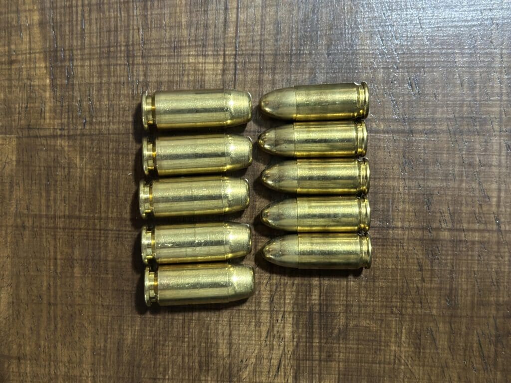 Five .40 S&W cartridges beside five 9mm Luger cartridges in two rows on a wooden table, showing the .40's wider flat-nose bullet