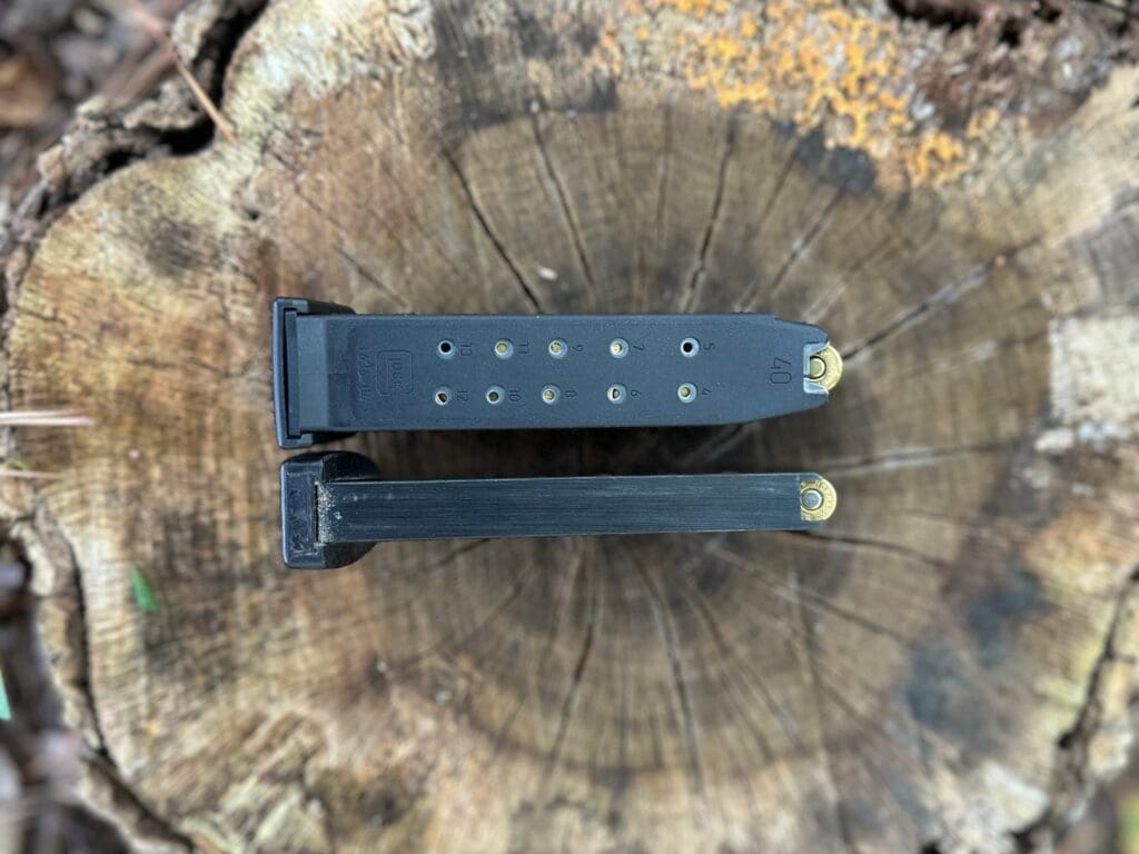 Glock 13-round .40 S&W magazine with rounds visible in its witness holes, beside a second loaded magazine on a tree stump